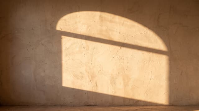 Sunlight through an arched window falling on a plaster wall