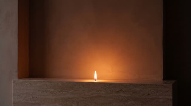 A small flame on a travertine ledge in a warm plaster niche