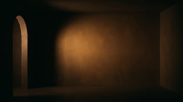 A dark room with an arched doorway and a soft pool of light on the wall
