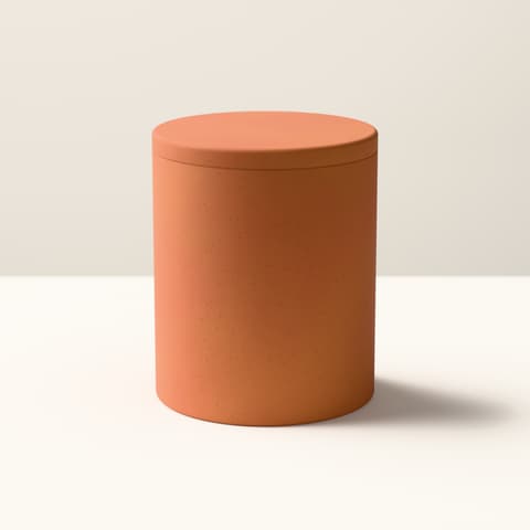 A matte terracotta-coloured cylindrical vessel with a flat lid, in bright midday light