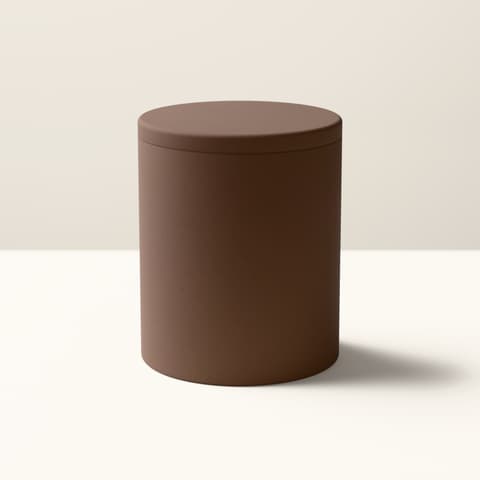 A matte walnut-coloured cylindrical vessel with a flat lid, in bright midday light